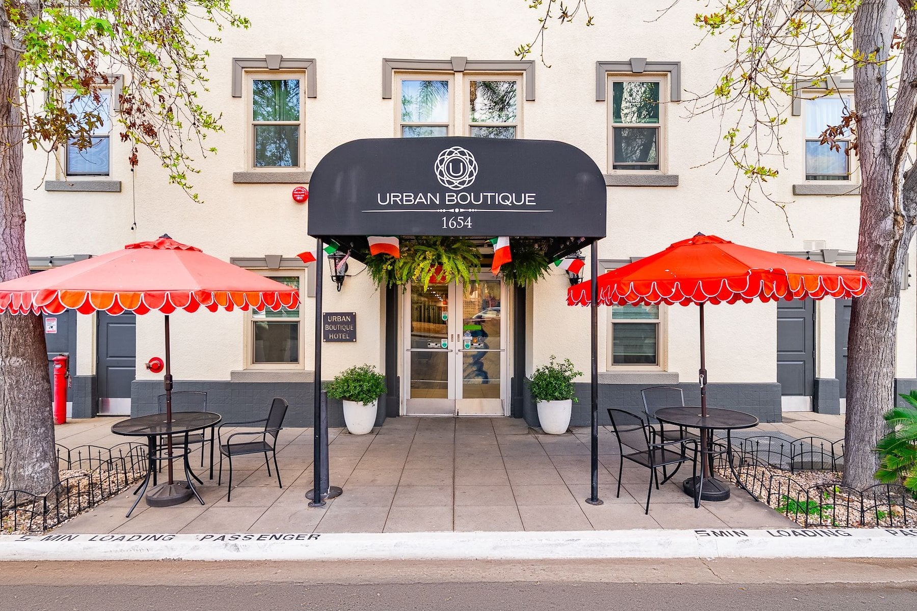 The main entrance of the Urban Boutique Hotel with a black awning, red umbrellas, and outdoor seating.